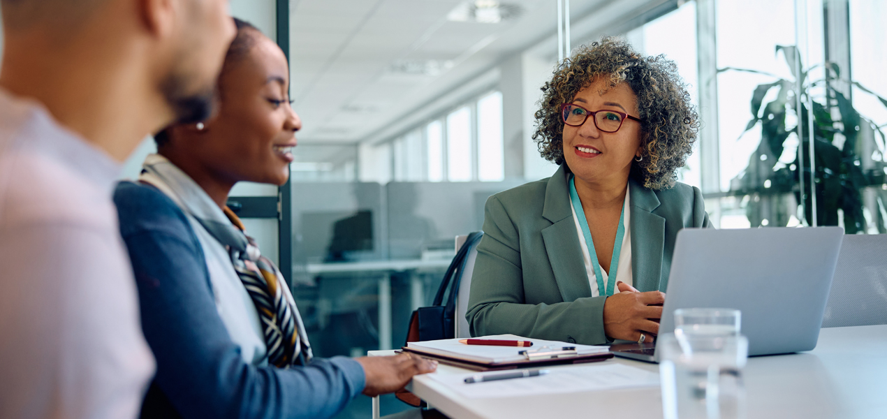 Deux personnes assises en face du bureau d’une autre personne en train de discuter.Deux personnes assises en face du bureau d’une autre personne en train de discuter.
