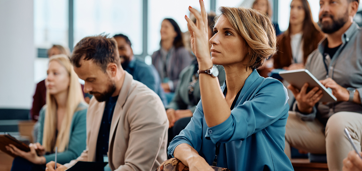 Dans une grande audience, une participante lève la main.