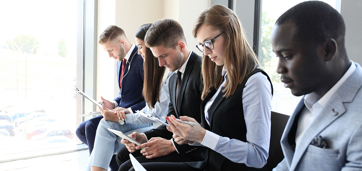 Une rangée de personnes assises attendant une entrevue, tenant leur CV et regardant leur téléphone.