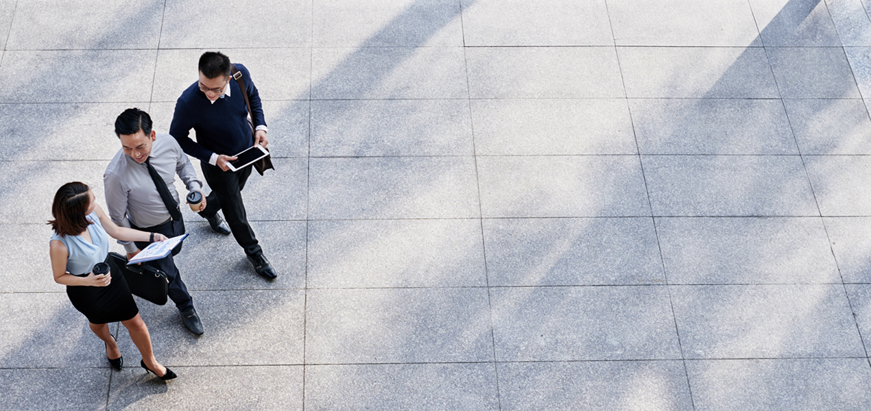 Vue aérienne de trois personnes en tenue d’affaires marchant à l’extérieur sur un pavé de pierre.