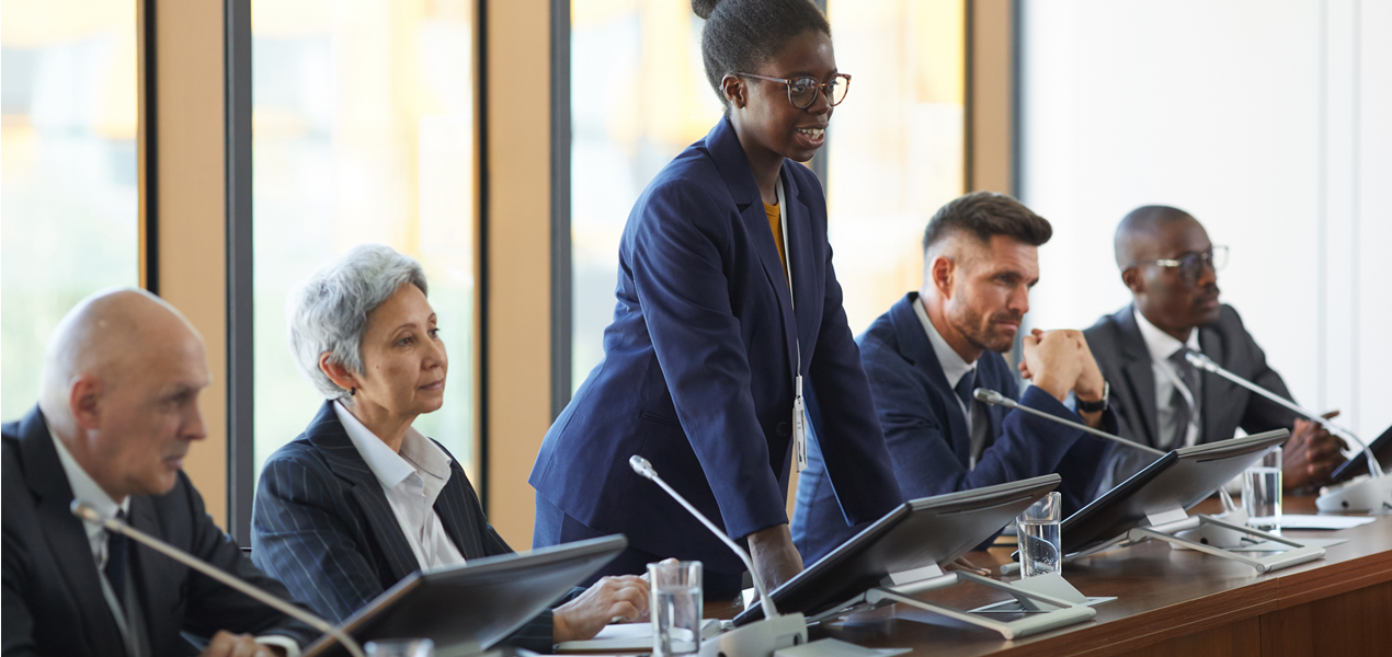 Un panel de cinq conférenciers avec une jeune femme se levant pour présenter.