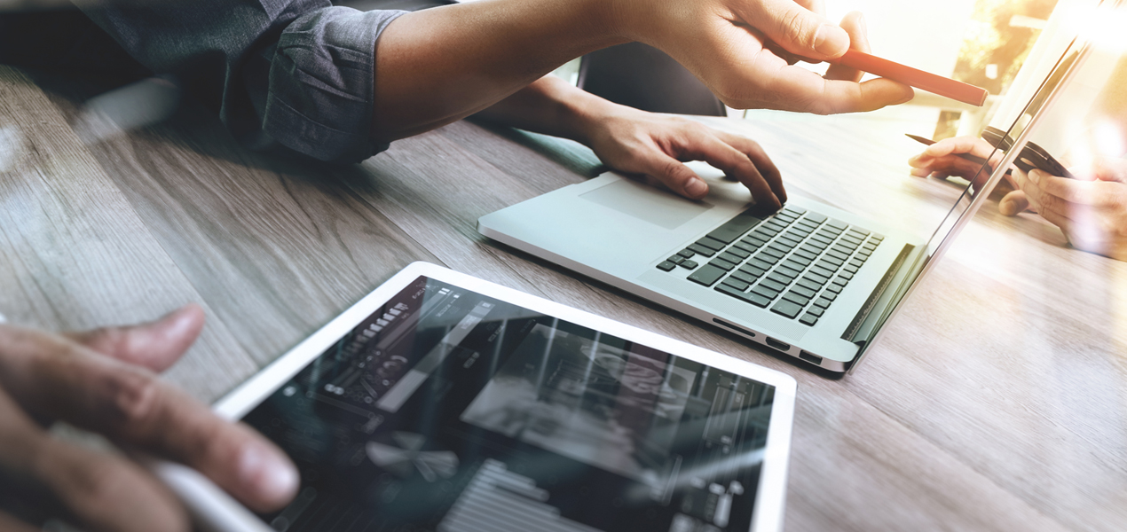 Gros plan sur les mains de deux personnes travaillant côte à côte, l’une utilisant une tablette et l’autre un ordinateur portable.