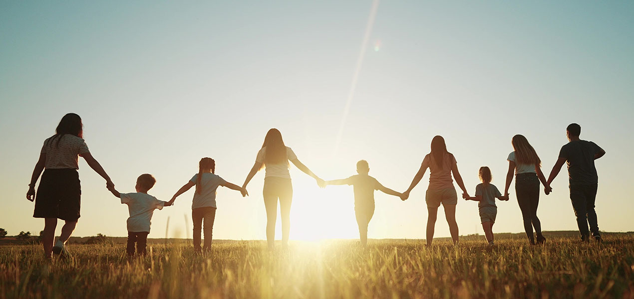 Les silhouettes d’un groupe d’adultes et d’enfants se tenant par la main dans le parc au coucher du soleil.